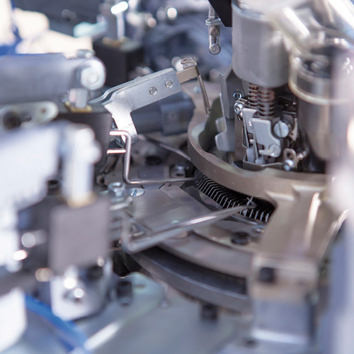 Close-up of intricate machinery with metal gears, levers, and springs, showcasing a complex mechanical system in silver and gray tones.