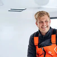 微笑的Oliver Heer穿着橙黑色救生衣在一艘白色船上,背景可见窗户。