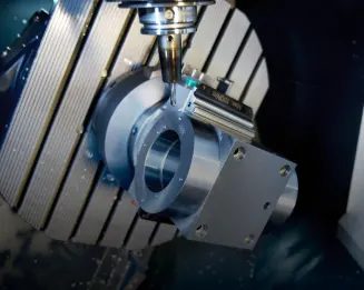 CNC milling machine cutting a metal workpiece on a slatted table with precision tooling and blue coolant visible