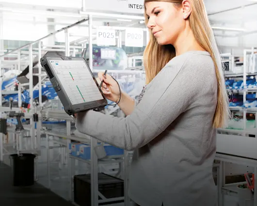 A woman is holding a tablet with digital assembly instructions in a modern manufacturing environment.