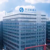 Modern glass office building with Huayan Robotics logo and Chinese text on rooftop against blue sky with white clouds.