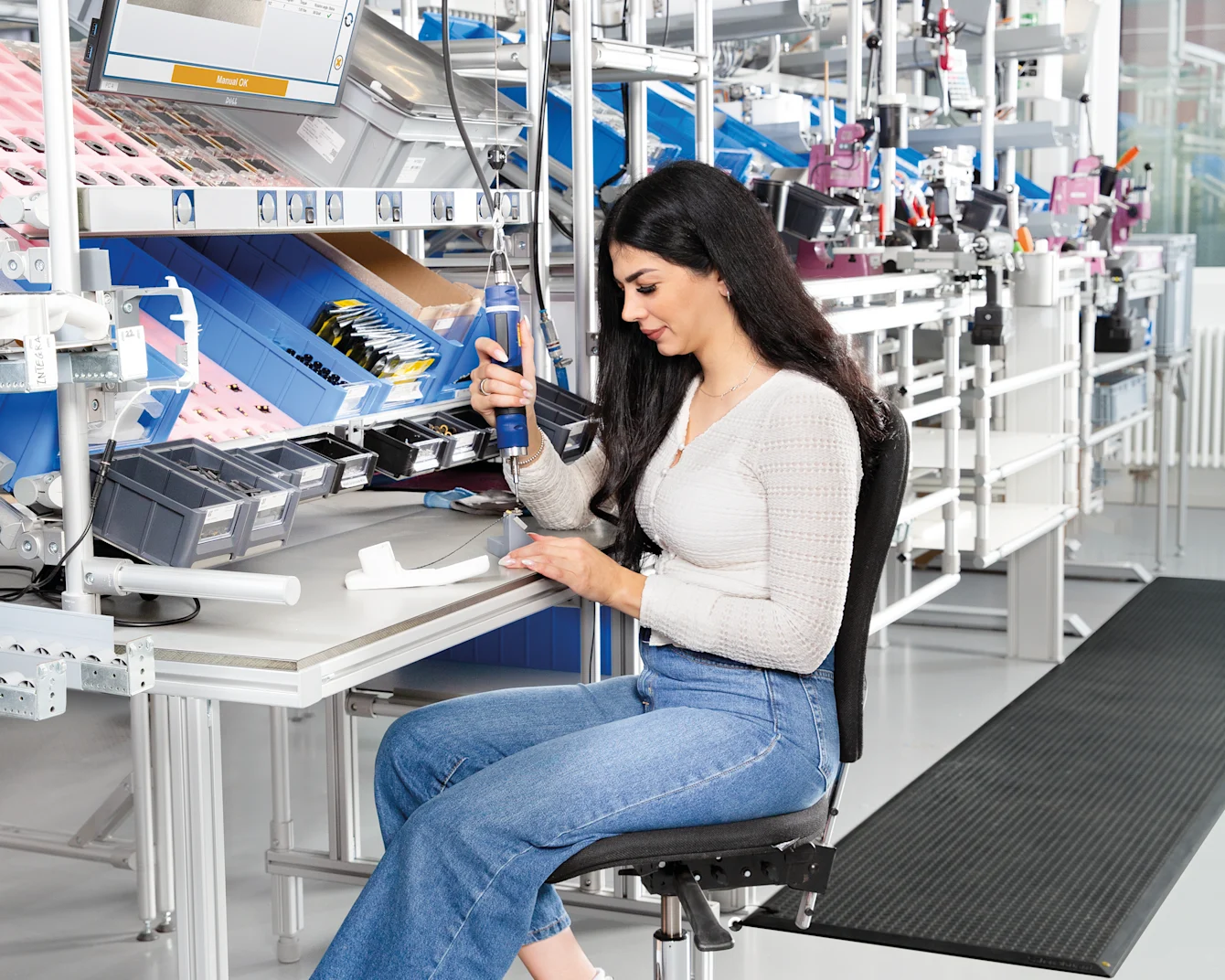 A woman sits at the workstation and assembles something with kolver tool