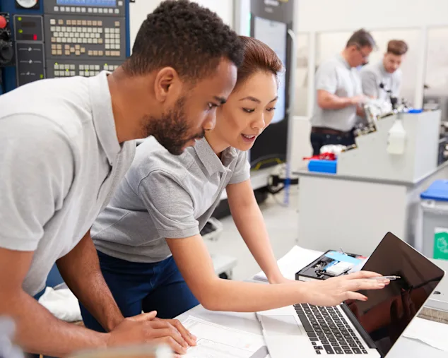 Two engineers chatting and reviewing test results together on a laptop in a technical laboratory.