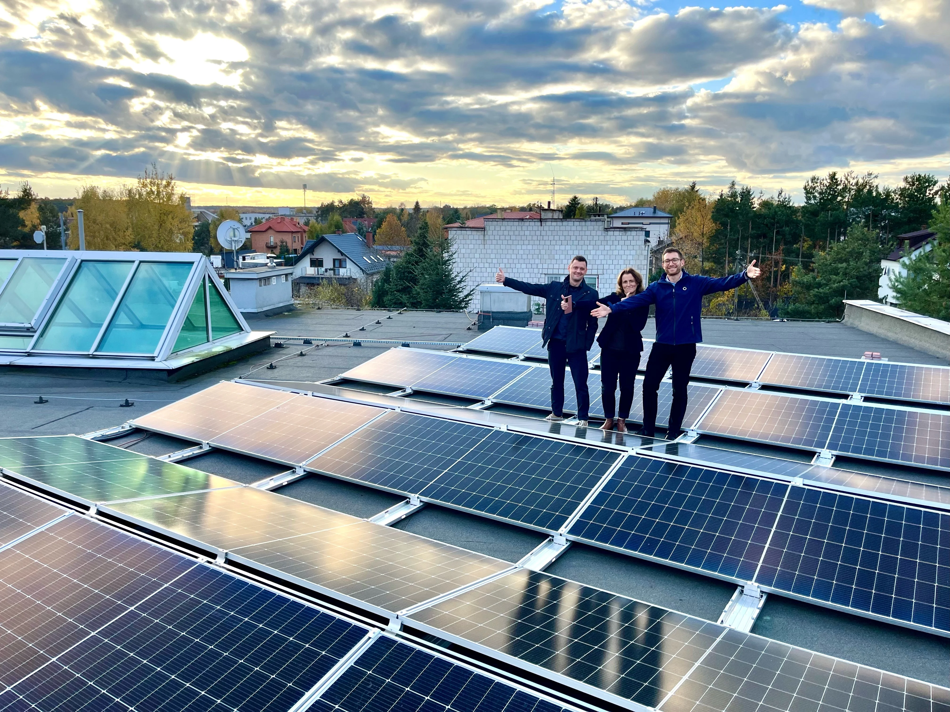 Three Bossard employees standing on a roof with solar panels with the sky and clouds in the background.