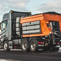 Epoke winter road maintenance equipment is on the road beside the snow-covered mountains.