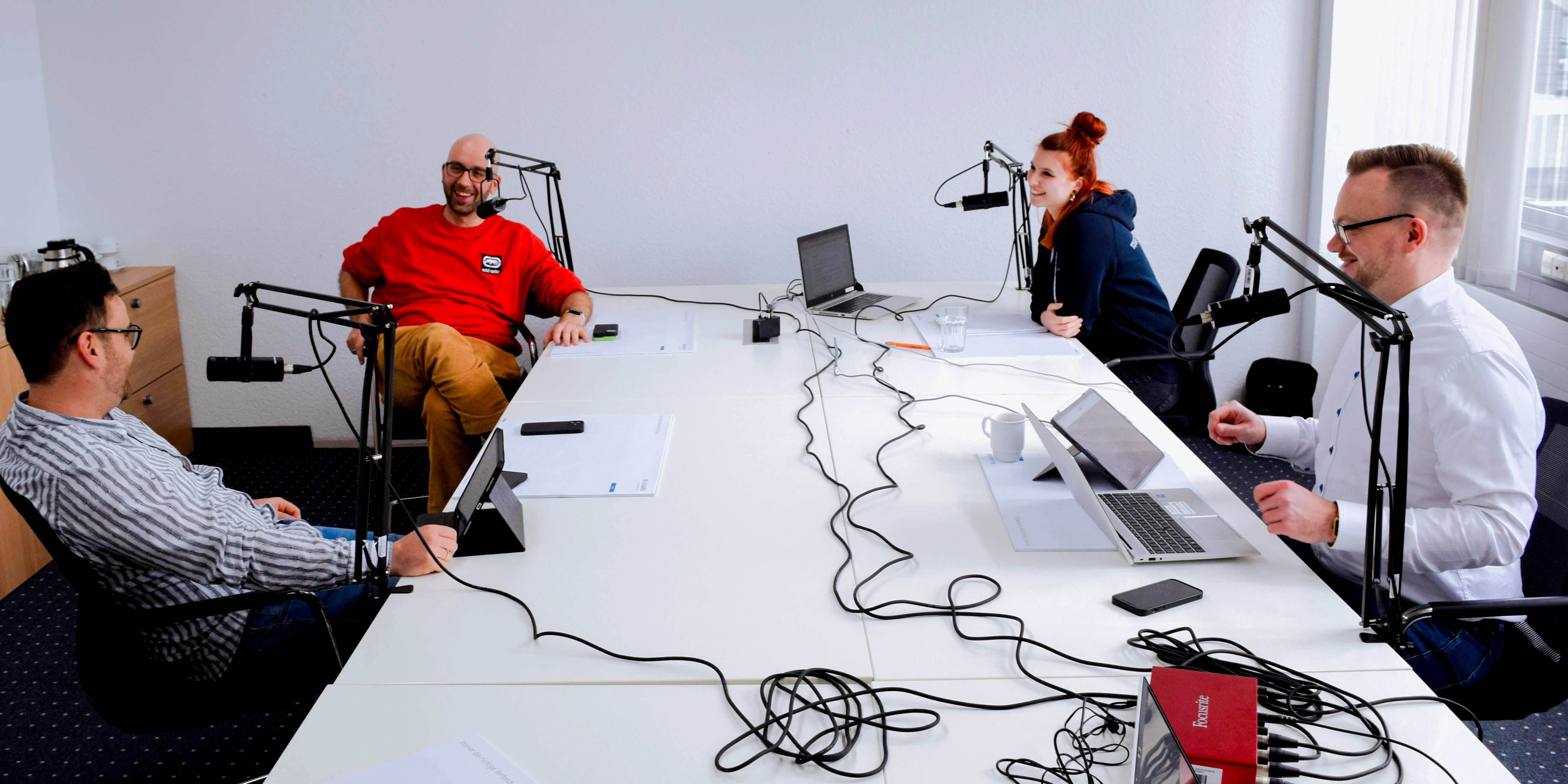 Four individuals seated at a table, each with a microphone, engaged in a discussion or interview setting.