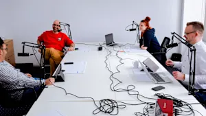 Four individuals seated at a table, each with a microphone, engaged in a discussion or interview setting.
