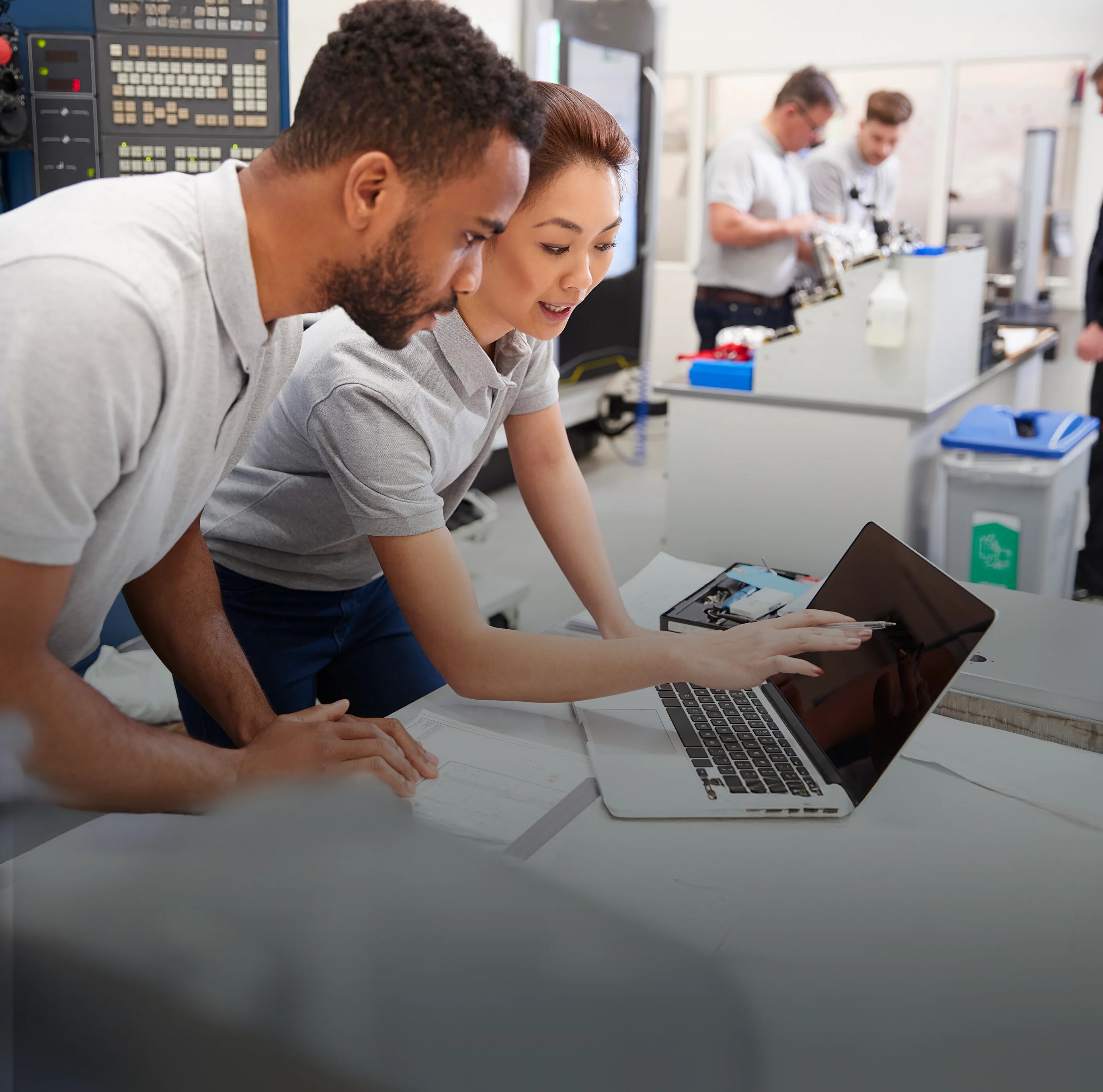 Two engineers chatting and reviewing test results together on a laptop in a technical laboratory.