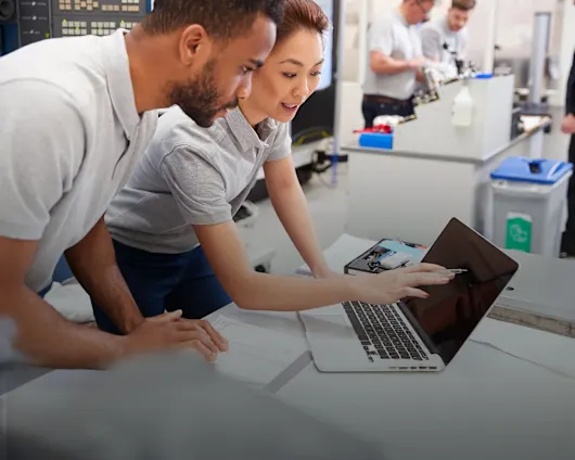 Two engineers chatting and reviewing test results together on a laptop in a technical laboratory.