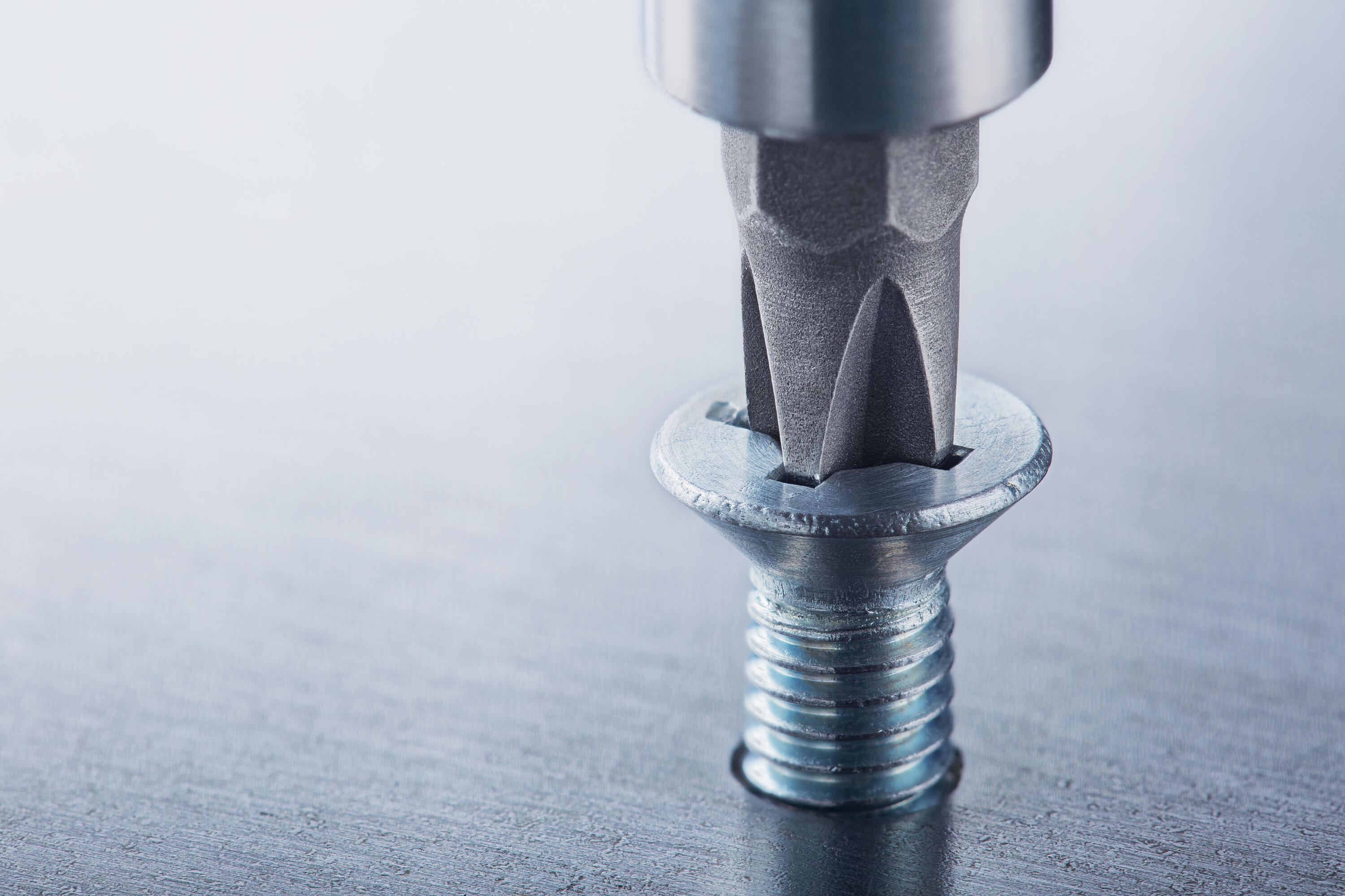 A screw with a cross recess drive is screwed into a metal plate.