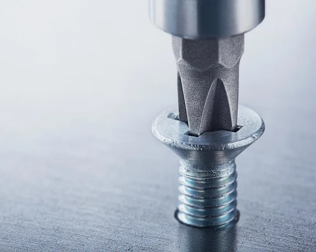 A screw with a cross recess drive is screwed into a metal plate.