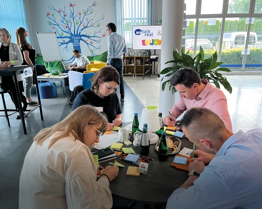 A group of individuals collaborates at a table, surrounded by colorful sticky notes, engaged in a brainstorming session.