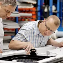 Two men collaborating on a train door assembly in a factory setting, focused on their tasks and surrounded by machinery.