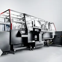 Large industrial machine with a sleek black and silver design, featuring a computer screen and red accents, on a gray background.