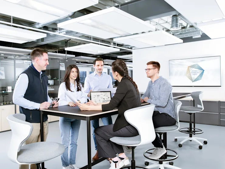 People around a table discussing a technical drawing in an industrial looking office. Key visual for Assembly Technology Expert Service only.