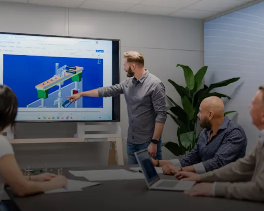 Two men reviewing CAD engineering drawings and 3D models on dual computer monitors in a modern office workspace.