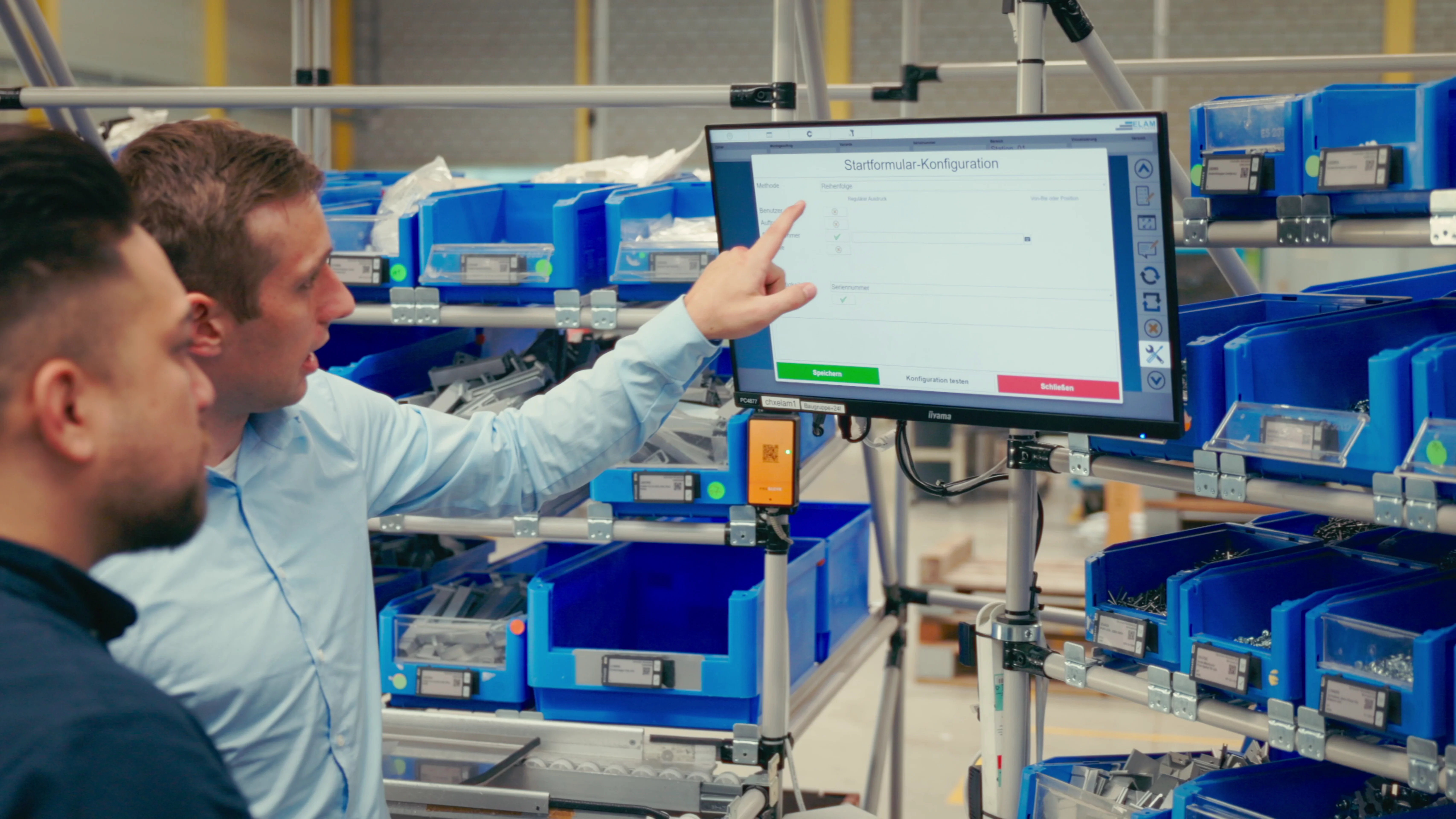 In a factory setting, two men focus on a computer screen, collaborating on tasks and analyzing data.