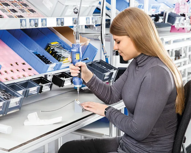 Woman sitting on workstation with connected kolver tool to assemble something.