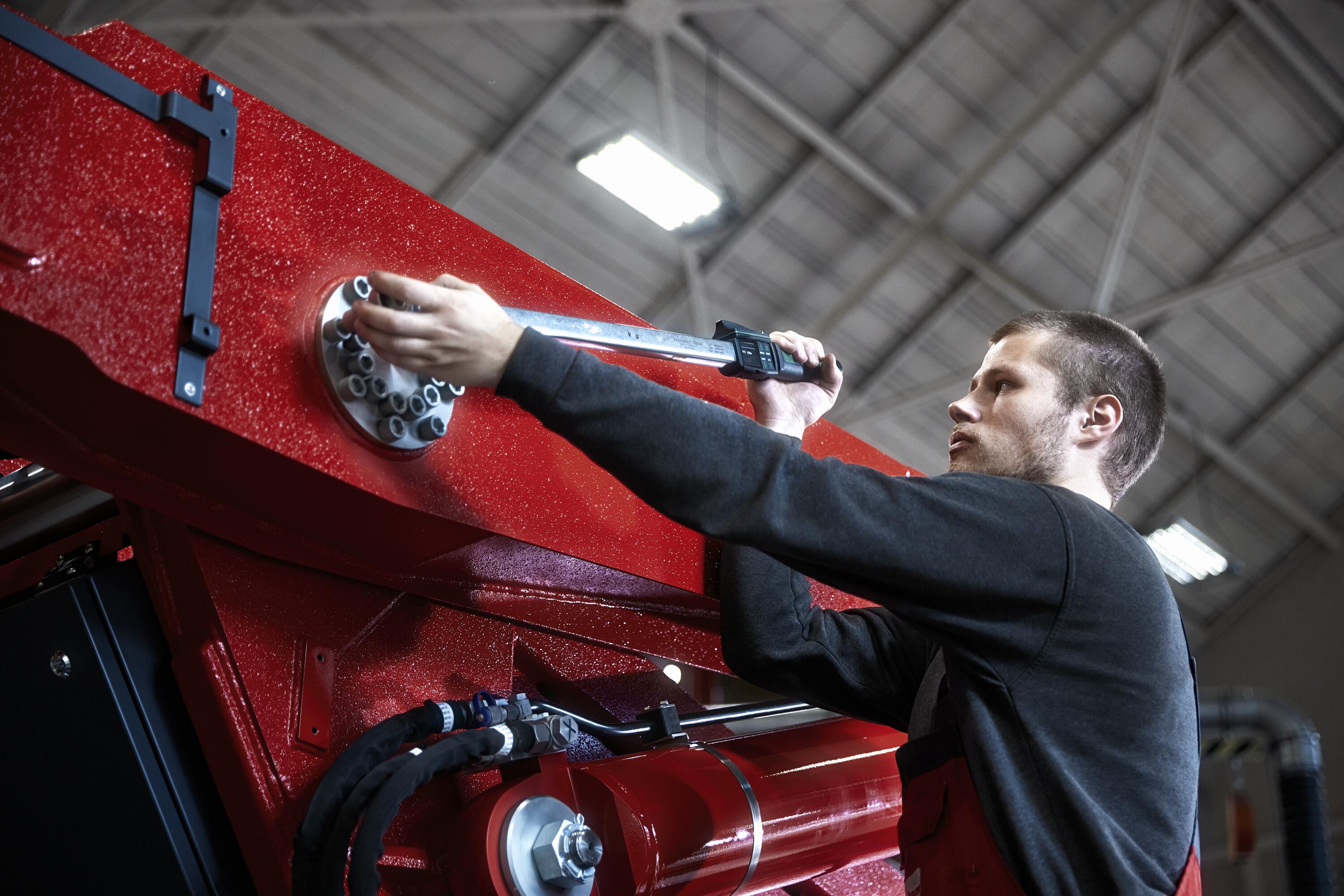 Maintenance worker in a black shirt tightens the screw of a heavy machine with a digital torque wrench.