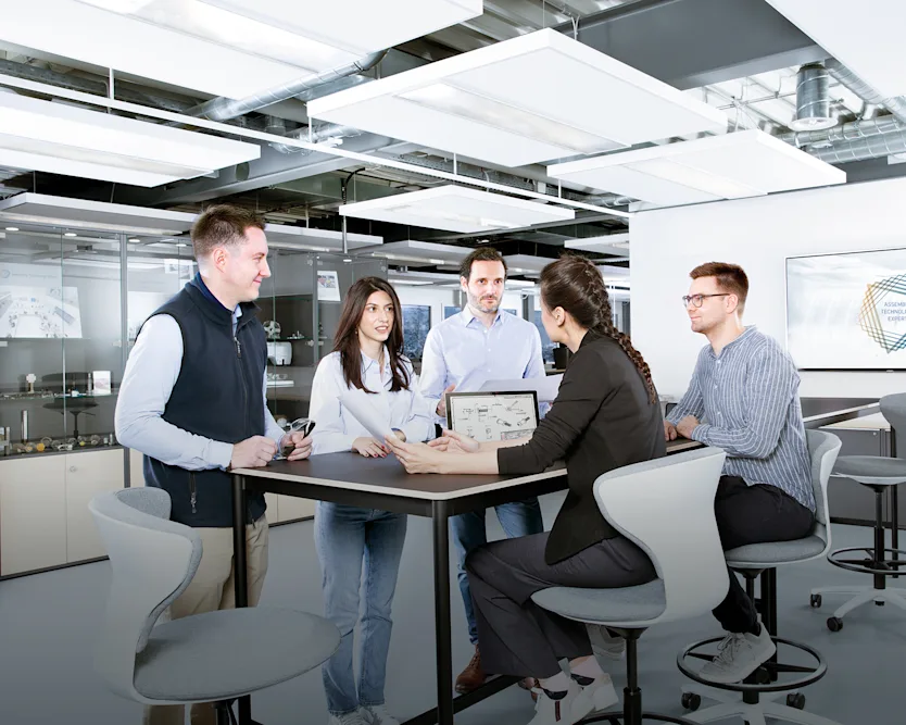 People around a table discussing a technical drawing in an industrial looking office.