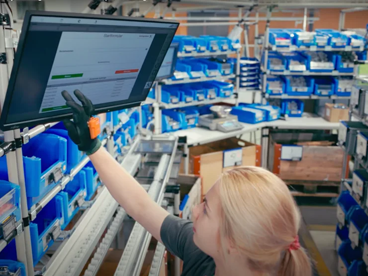 Young assembly worker checking work instructions on a computer screen with Bossard SmartBins in the background.