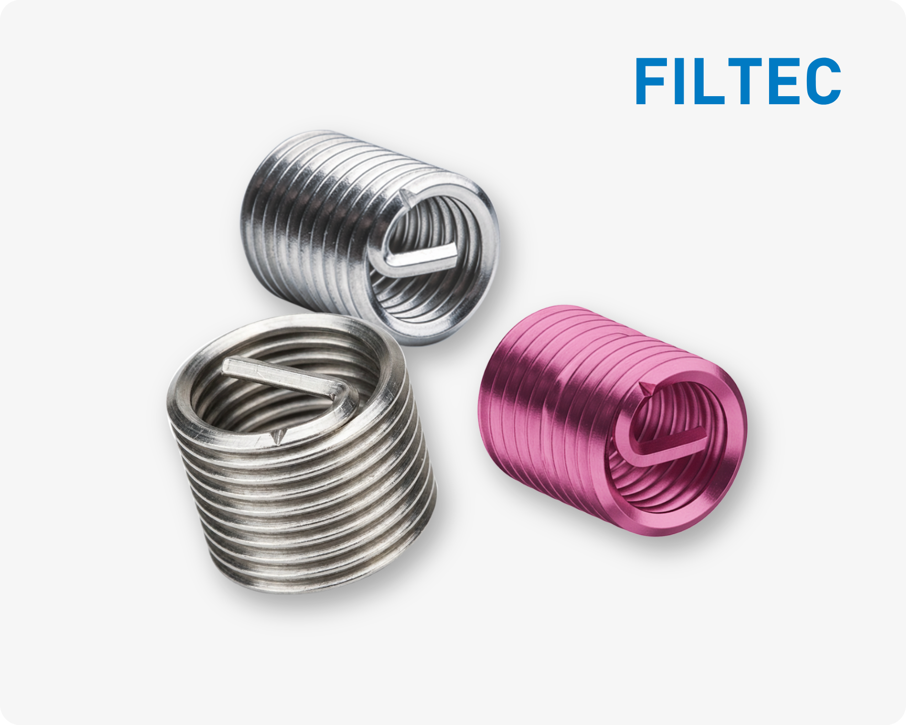 Three FILTEC wire thread inserts, in silver and one pink, with spiral structure on a light grey background and FILTEC logo in the top right corner.