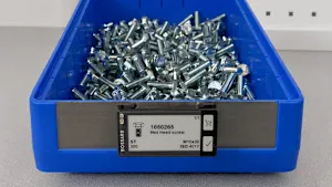 Blue plastic storage bin filled with metal hex head screws, with a smart label showing product number and size.