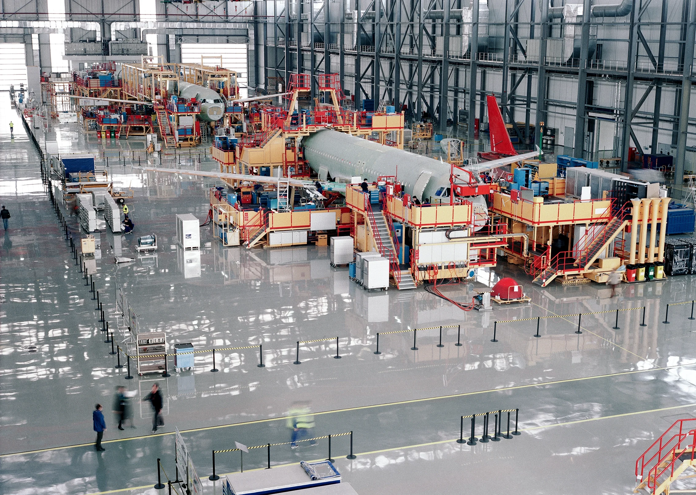 A large airplane is being assembled inside a spacious factory, showcasing industrial machinery and workers in the background.