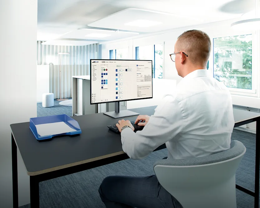 A man seated at a desk, focused on his computer screen, engaged in work.