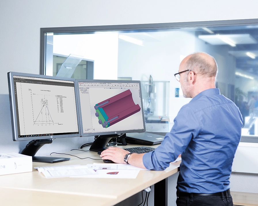 A man in a blue shirt works on a technical drawing at a standing desk on a computer