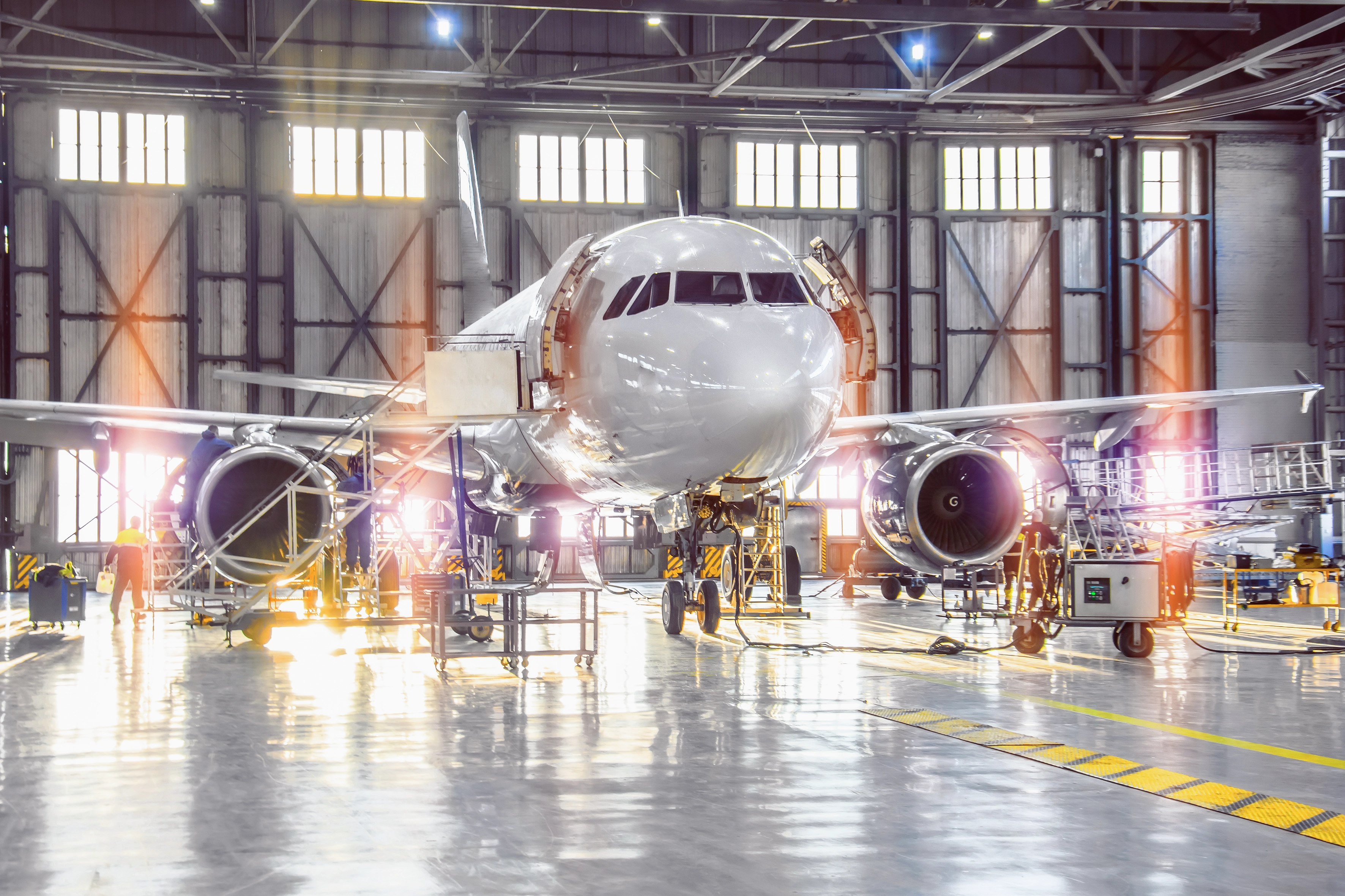 An airplane undergoing maintenance inside a spacious hangar, with technicians and tools visible around it.