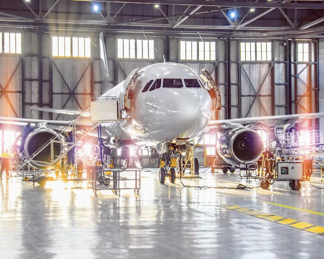 An airplane undergoing maintenance inside a spacious hangar, with technicians and tools visible around it.