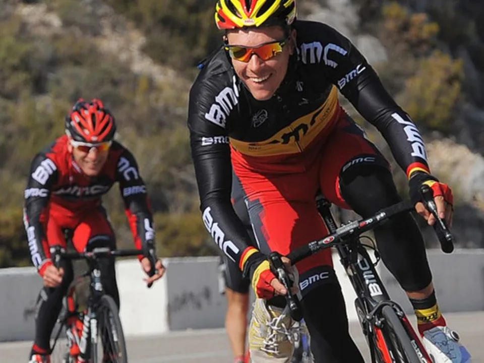 Three men dressed in red and black jerseys with BMC logo cycling together, highlighting their shared passion for biking.