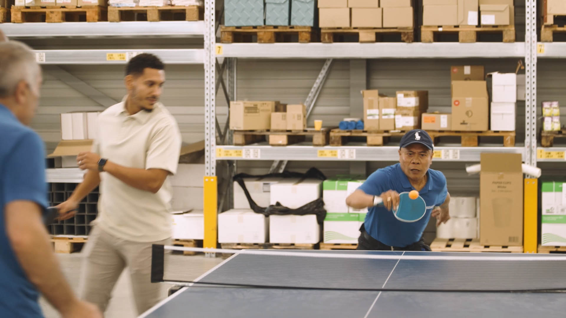 A  men is engaged in a competitive game of ping pong inside a spacious warehouse setting.