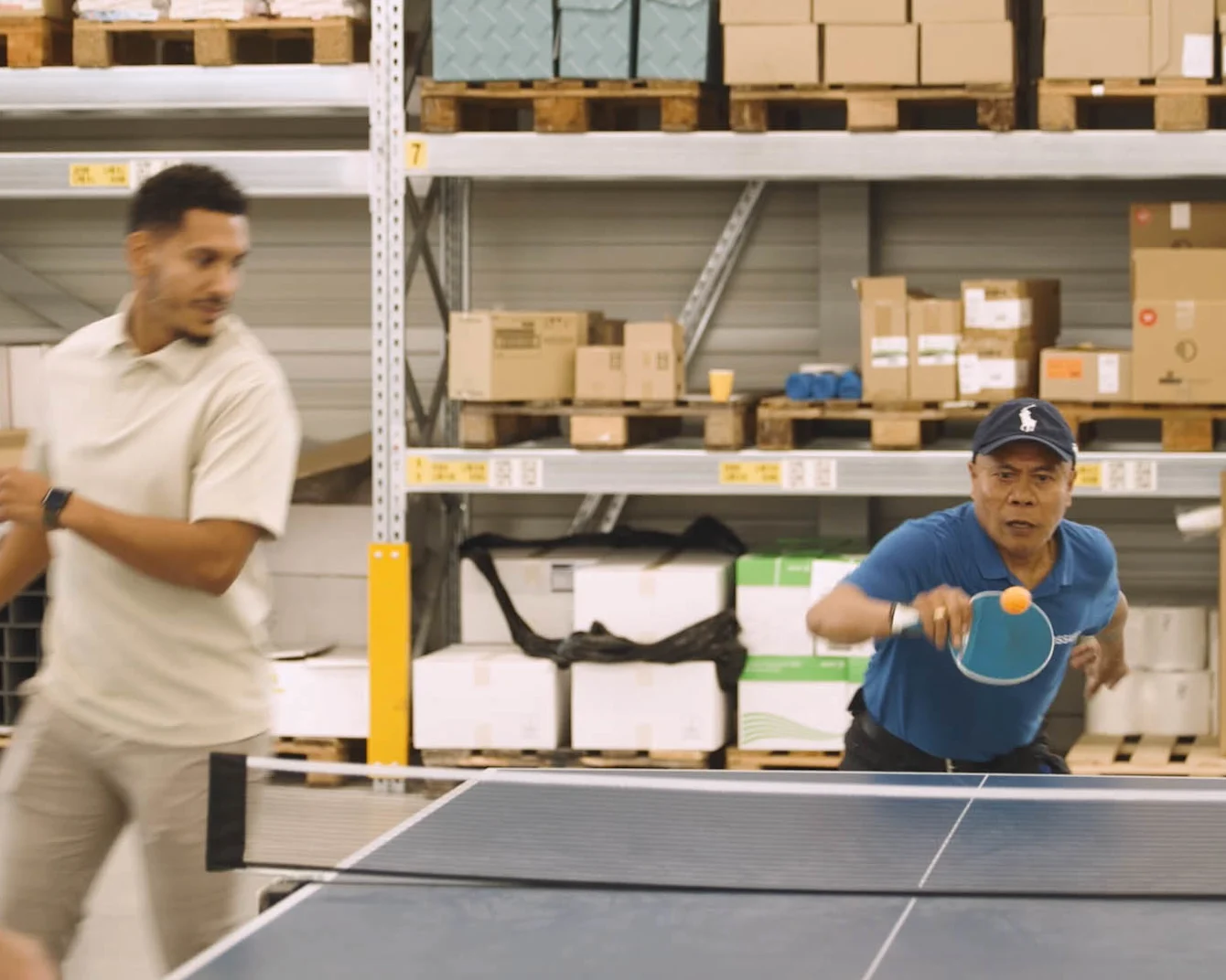 A men is engaged in a competitive game of ping pong inside a spacious warehouse setting.