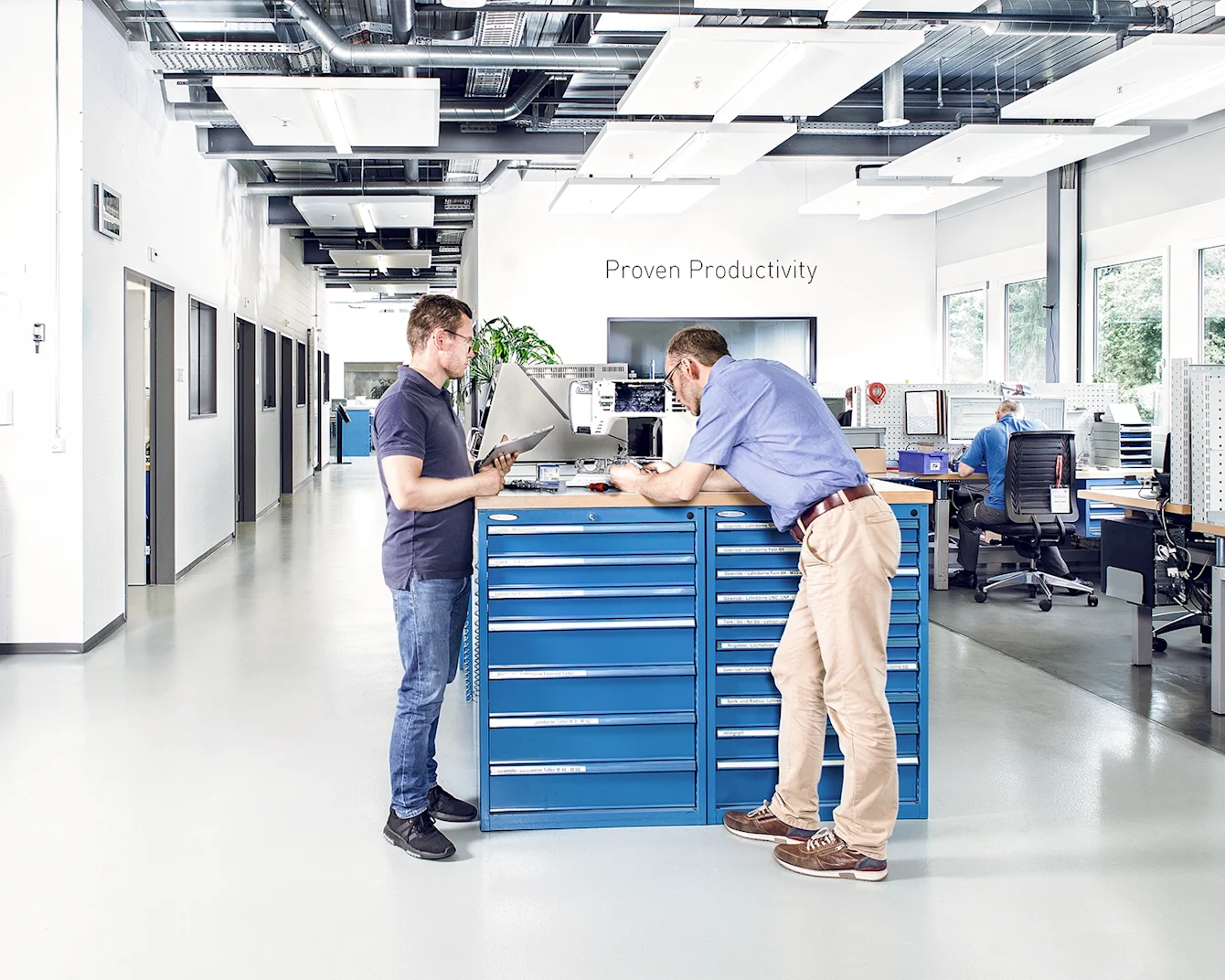 Two men in a test lab examine a sewing machine on a desk in an industrial lab with additional workstations in the background. Key visual for Expert Test Services.