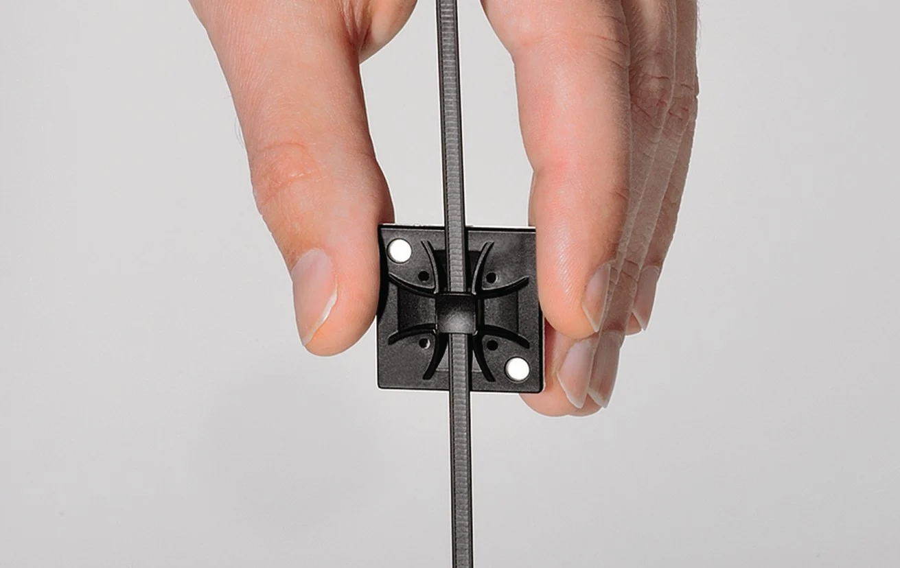Hand holding a black HellermannTyton Q-Mount Cable Mounting to fix cable ties into place