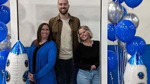 Three people pose together in a photo frame of a Bossard Americas social media post, surrounded by silver and blue balloons.