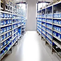 A warehouse aisle with metal shelves filled with blue bins, containing various small parts and tools, under bright lighting.