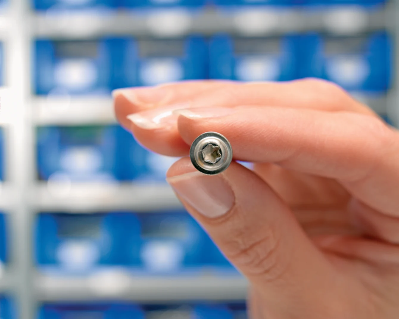 Female hand holding a hexalobular socket pan washer head screw in front of a background with blue boxes