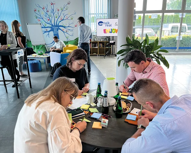 A group of individuals collaborates at a table, surrounded by colorful sticky notes, engaged in a brainstorming session.
