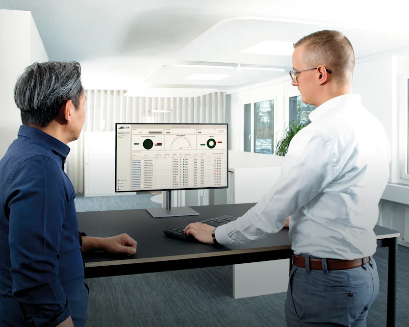 Two men at a desk, focused on a computer screen displaying a data report.
