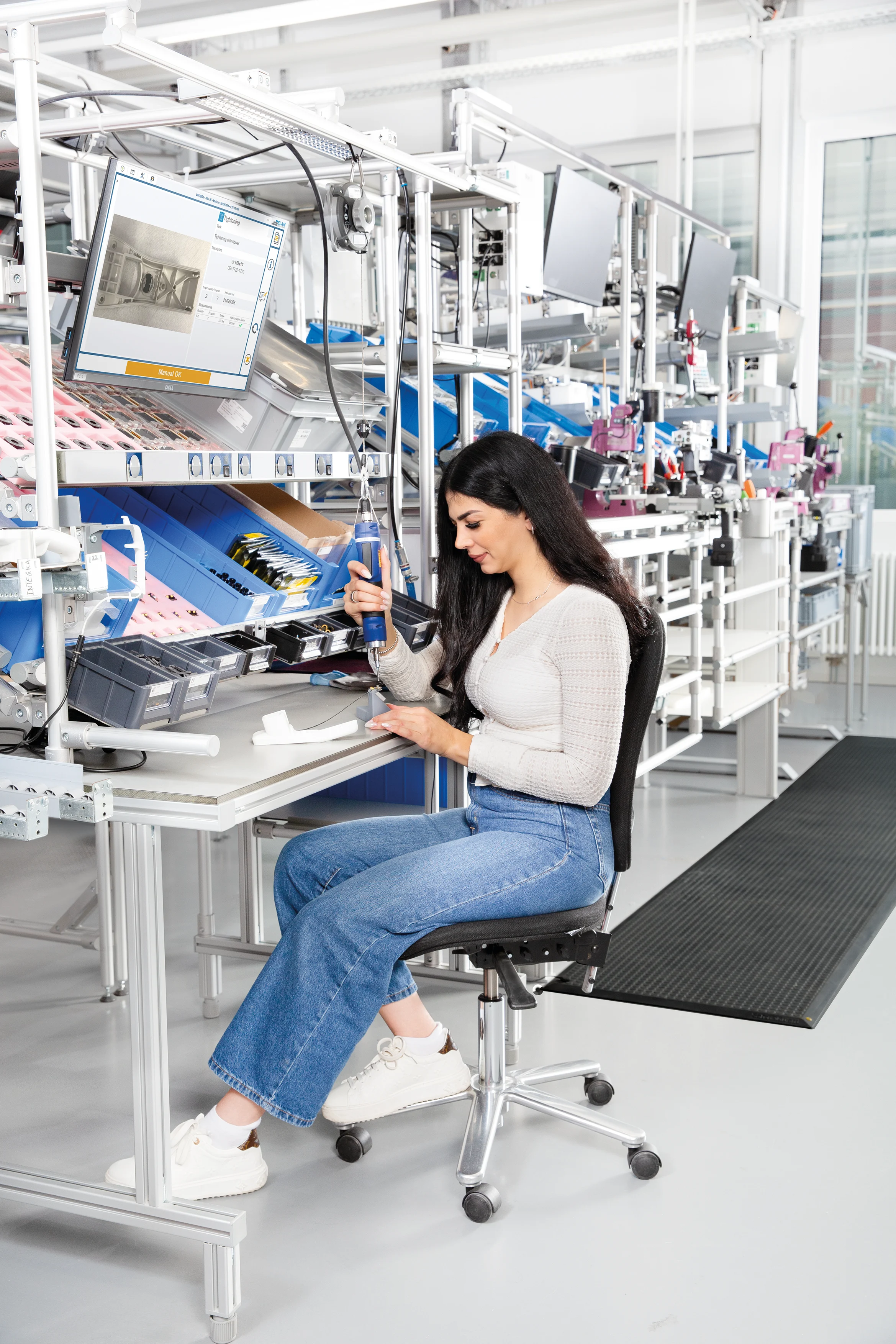 A woman sits at the workstation and assembles something with kolver tool