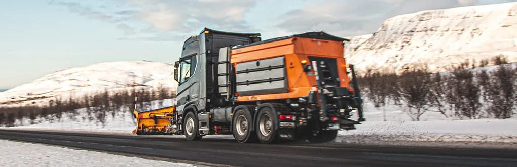 Epoke winter road maintenance equipment is on the road beside the snow-covered mountains.