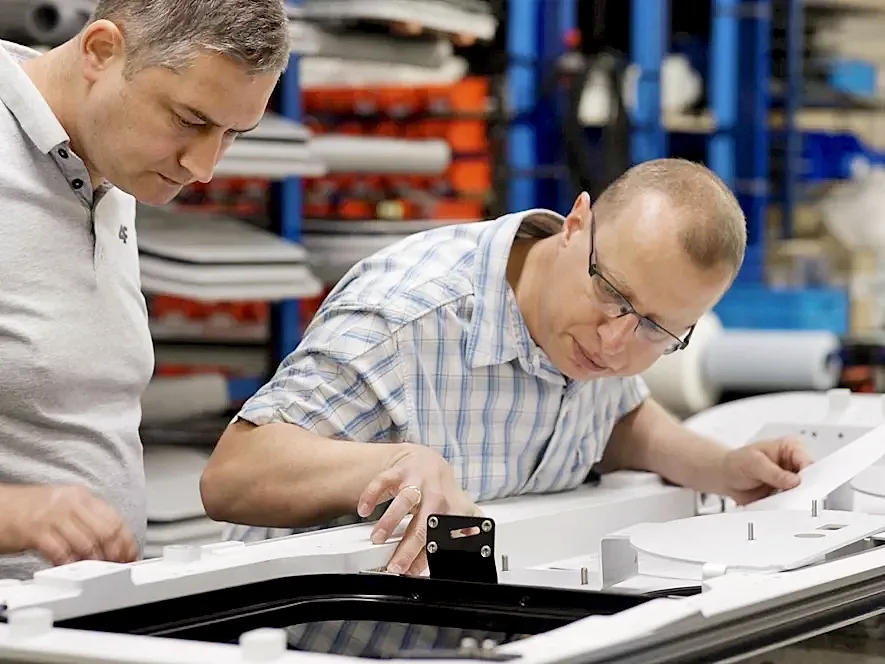 Two men collaborating on a train door assembly in a factory setting, focused on their tasks and surrounded by machinery.