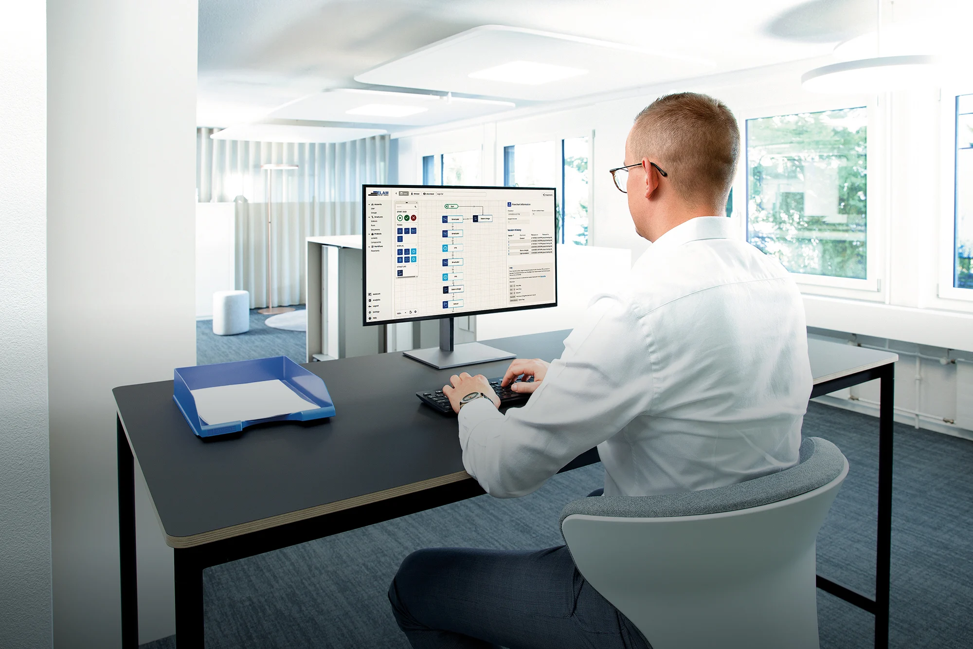 A man seated at a desk, focused on his computer screen, engaged in work.