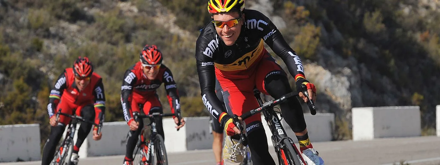 Three men dressed in red and black jerseys with BMC logo cycling together, highlighting their shared passion for biking.