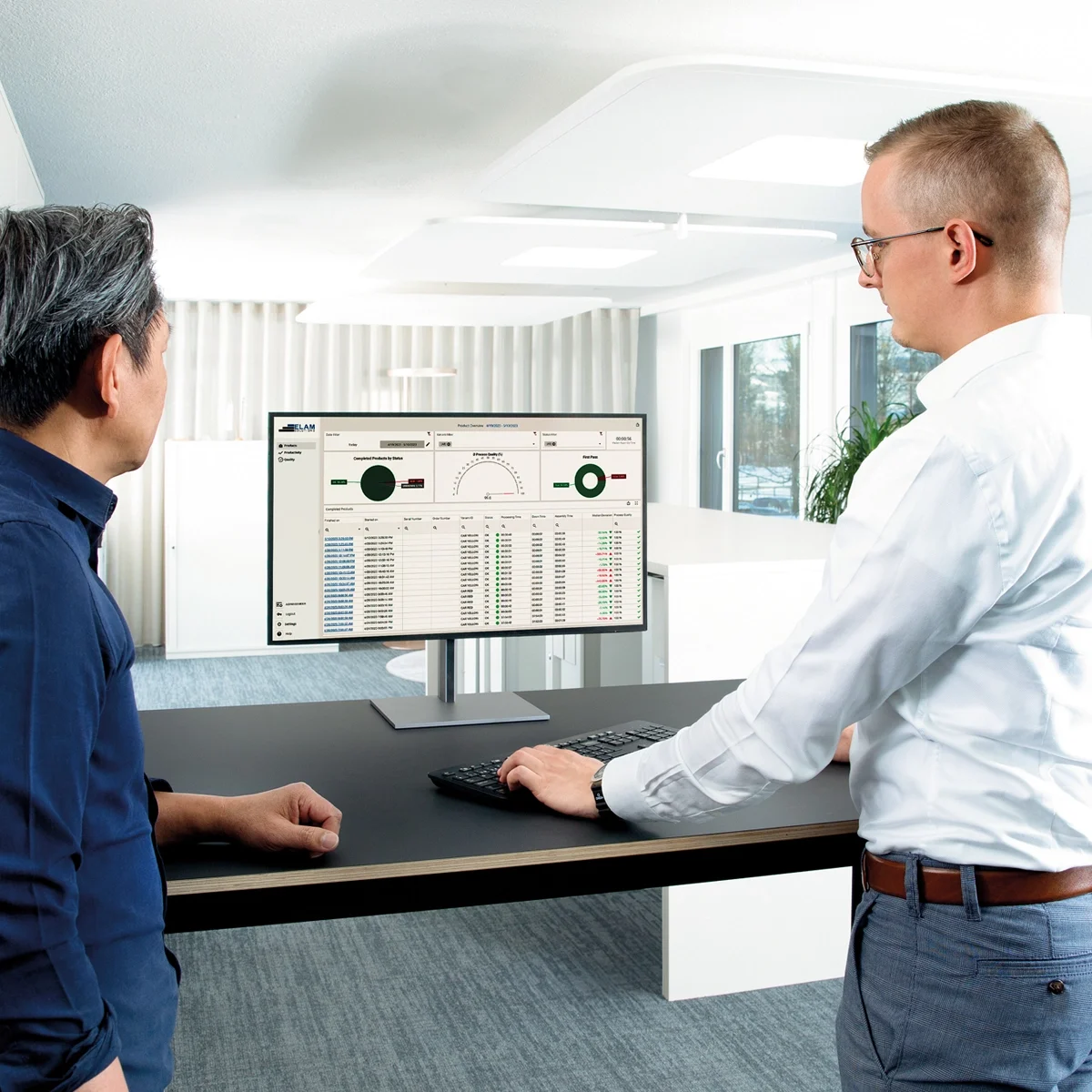 Two men at a desk, focused on a computer screen displaying a data report.